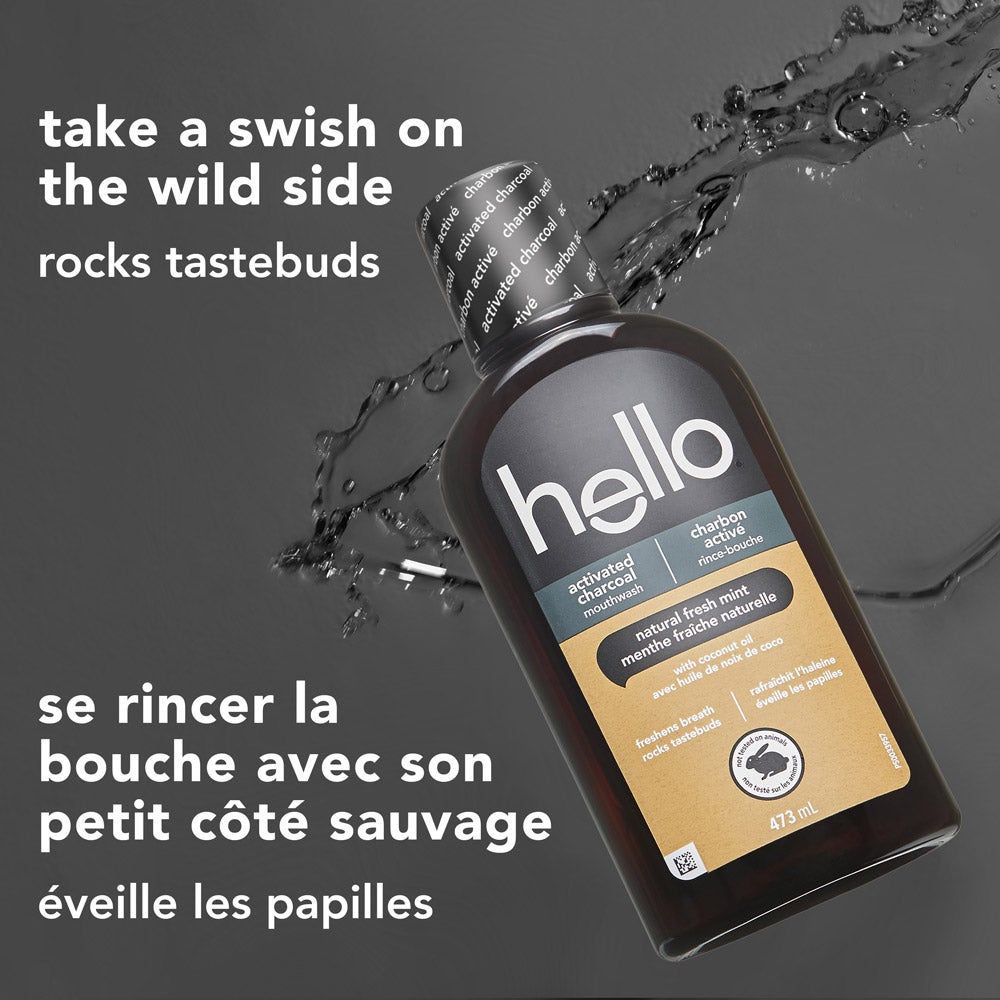 A black bottle of hello activated charcoal mouthwash is tilted on its side with water droplets splashing nearby, set on a dark background. The text above reads: "take a swish on the wild side – rocks tastebuds."